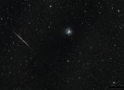 A meteor streaks past the Iris Nebula.