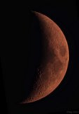 A detailed shot of a crescent moon turned red by smoke from forest fires.